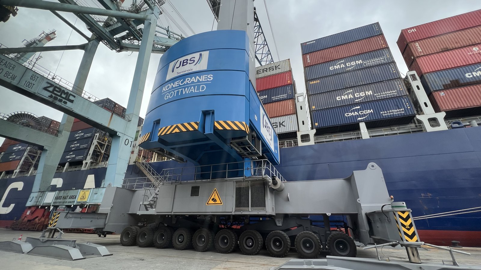 Grúa portuaria móvil azul operando junto a un buque portacontenedores
